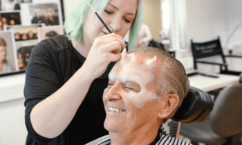 Hair and makeup artist creating a look for film, happy man smiling